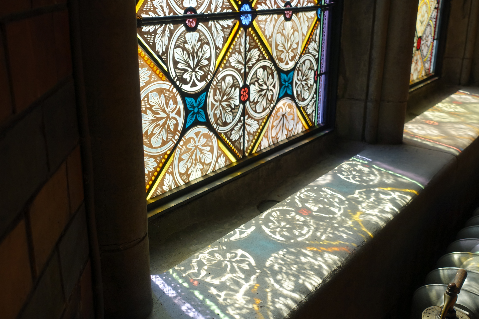 Bild på glasfönster där solen lyser in och reflekterar mönstret på fönsterbrädan