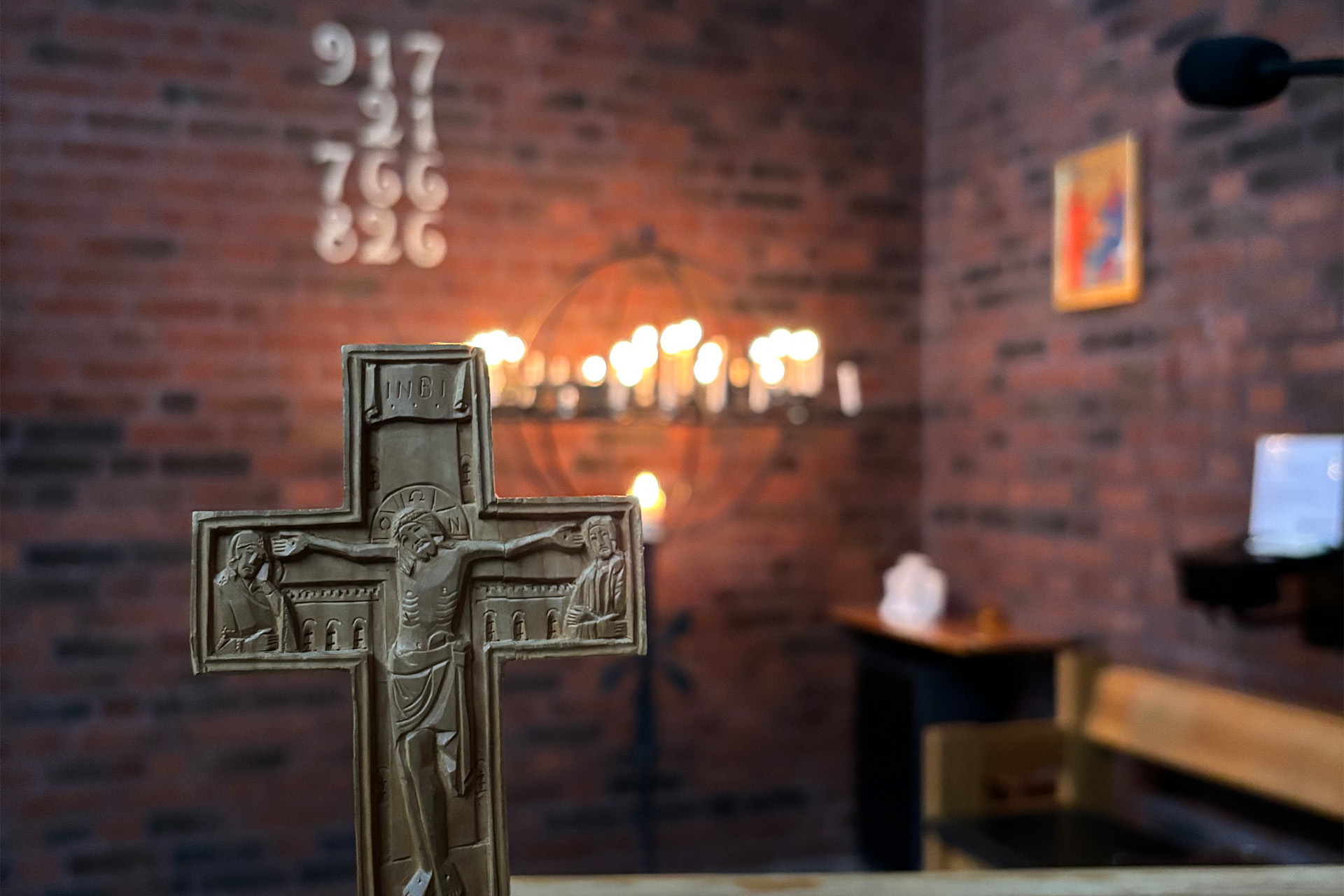 Bild på kors i Guldhedskyrkan framför tegelvägg och ljusbärarare med tända ljus.