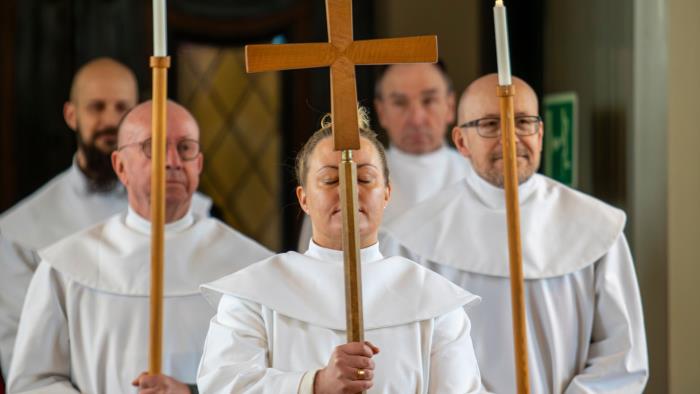 Fyra män och en kvinna i vita kåpor bär kors och ljus.