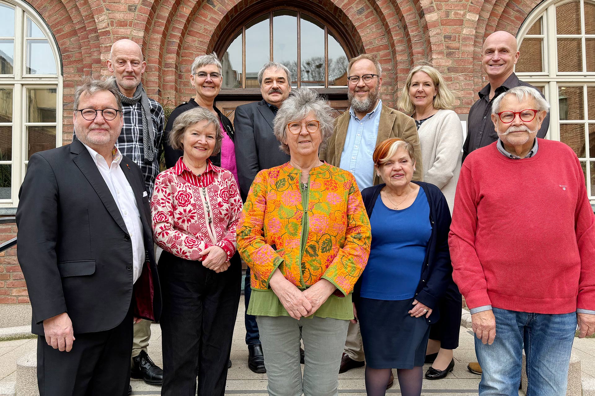 Gruppbild av män och kvinnor framför en port.