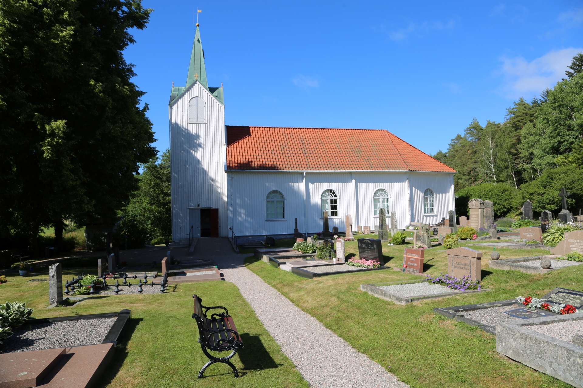 En vit träkyrka med torn, omgiven av en kyrkogård med gravstenar.