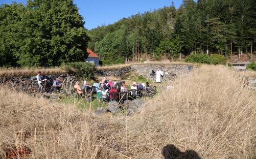 En grupp människor sitter på platststolar i en ruin. Framför dem står en präst vid ett stenaltare.