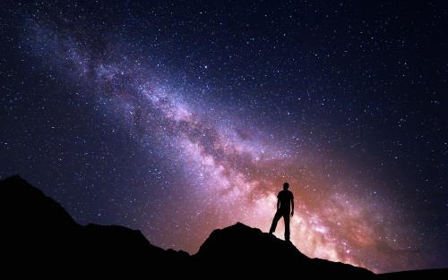 Person står på ett berg och tittar upp på stjärnhimlen