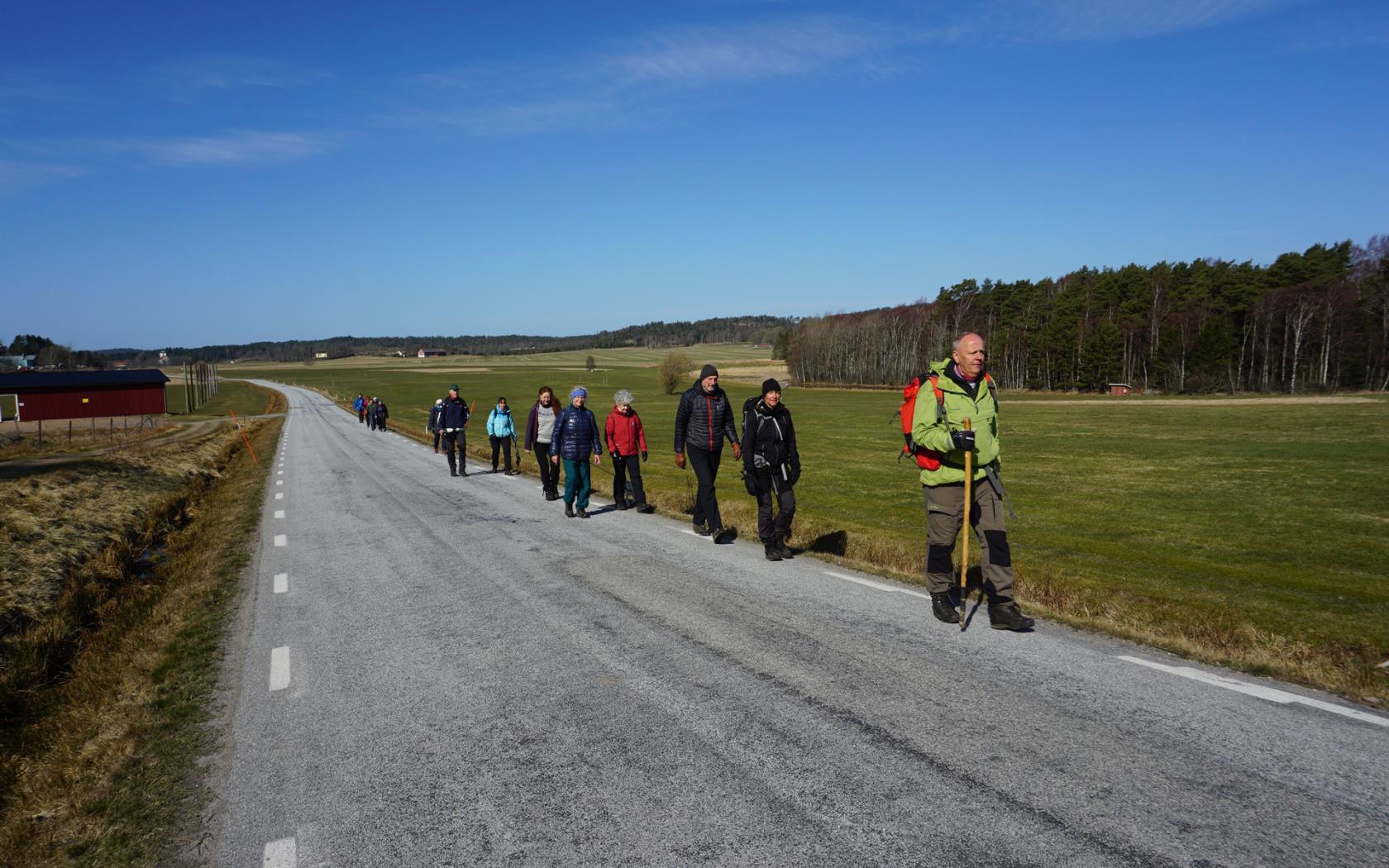 Pilgrimmer på vandring längs en landsväg. Soligt väder och blå himmel. 