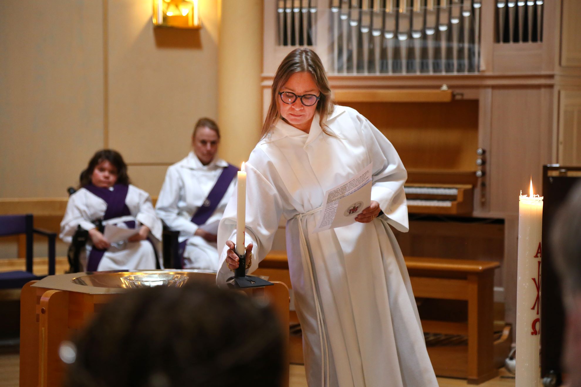 En kvinnlig präst tänder ett ljus under en gudstjänst i en kyrkolokal.