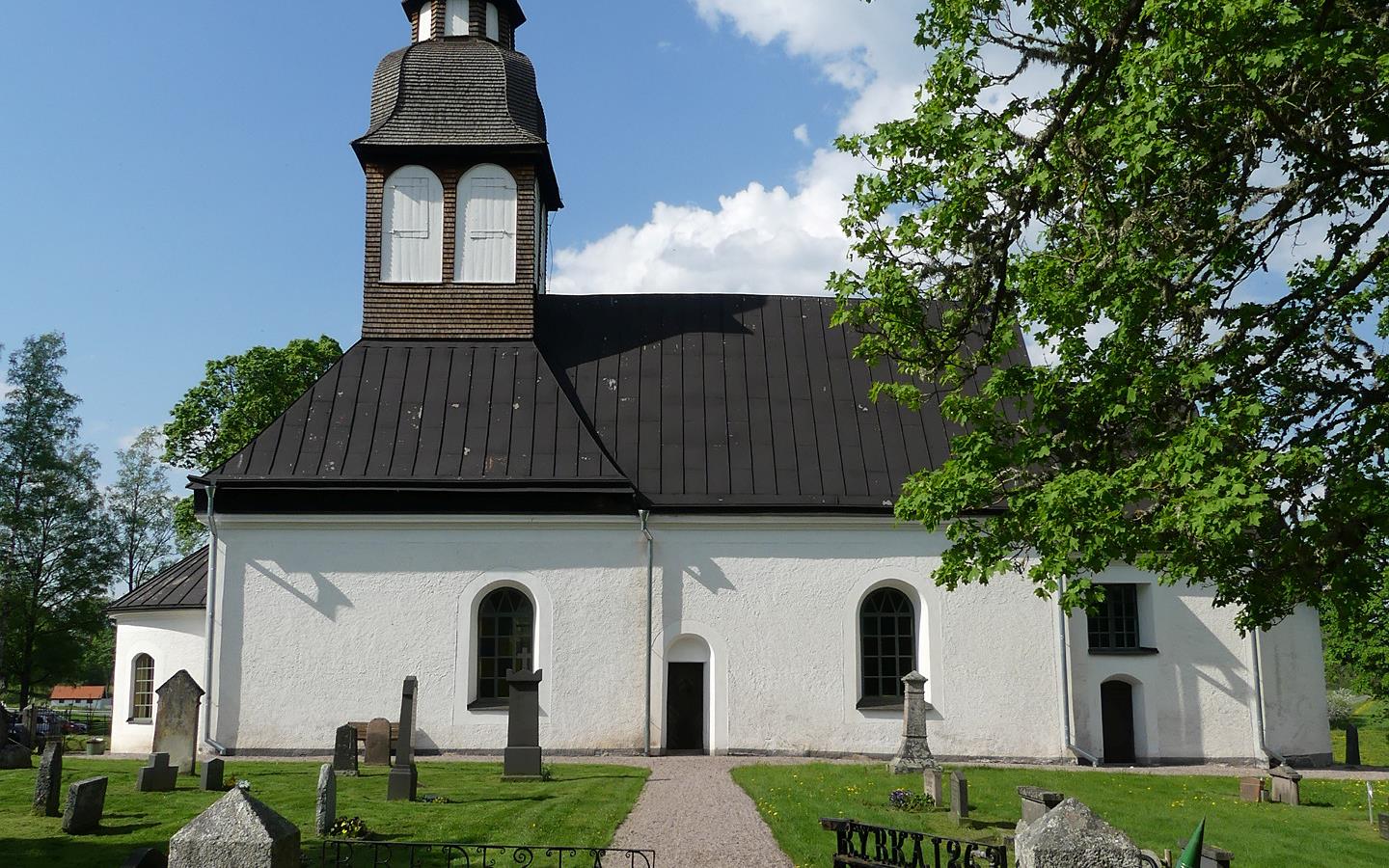 Längst fran i bild en öppen grind in till kyrkan som vi ser längst bak i bild. 