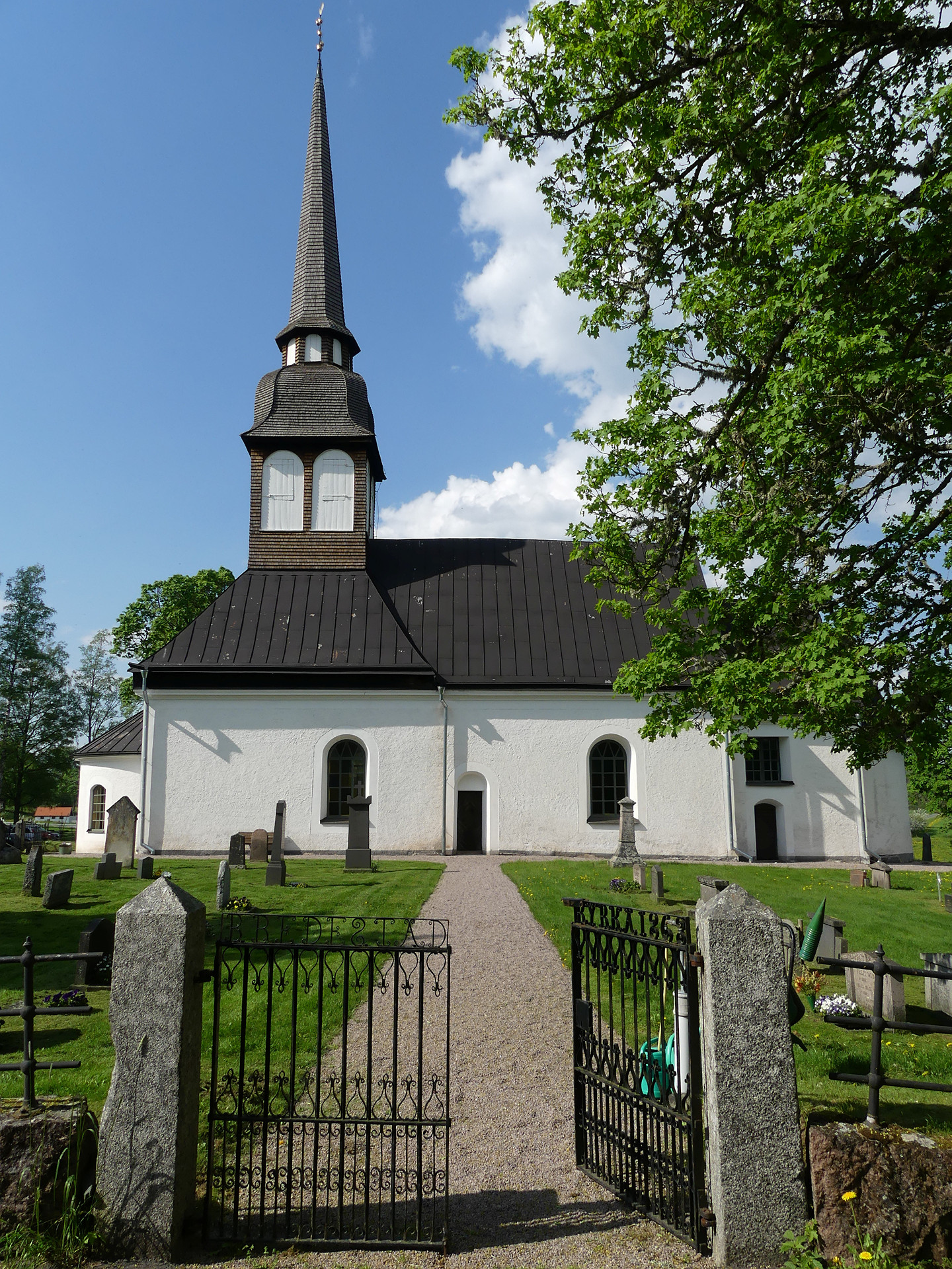 Längst fran i bild en öppen grind in till kyrkan som vi ser längst bak i bild. 