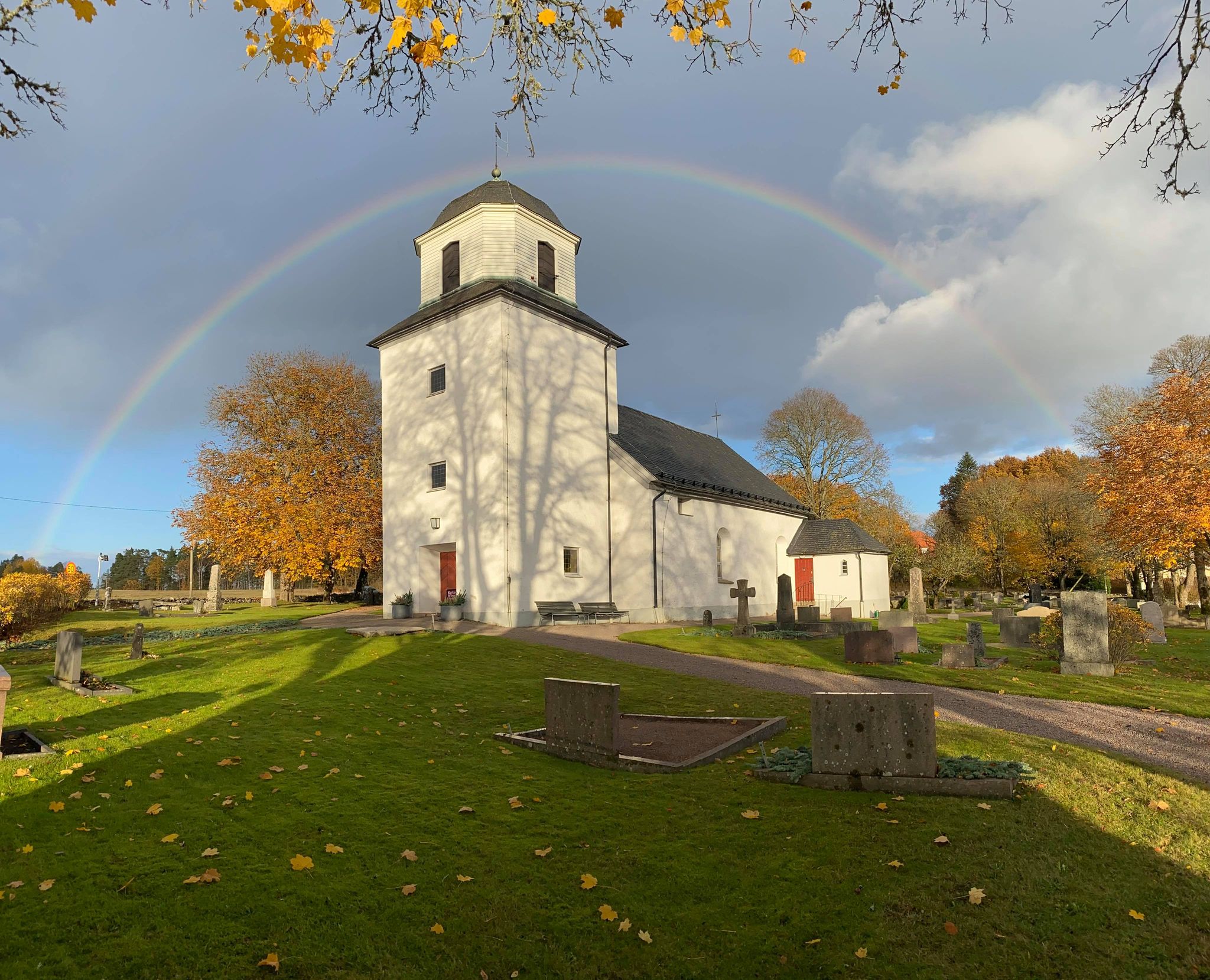 En regnbåge spänner över hela Östad kyrka, i höstsol.