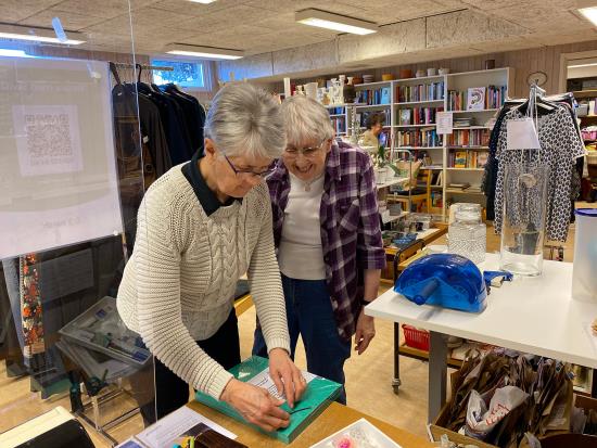 Två äldre damer packar upp skänkta saker till secondhandbutiken.