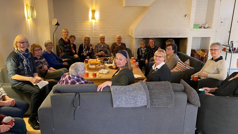 Ett stort antal glada äldre damer sitter i soffor och fåtöljer runt kaffebordet.