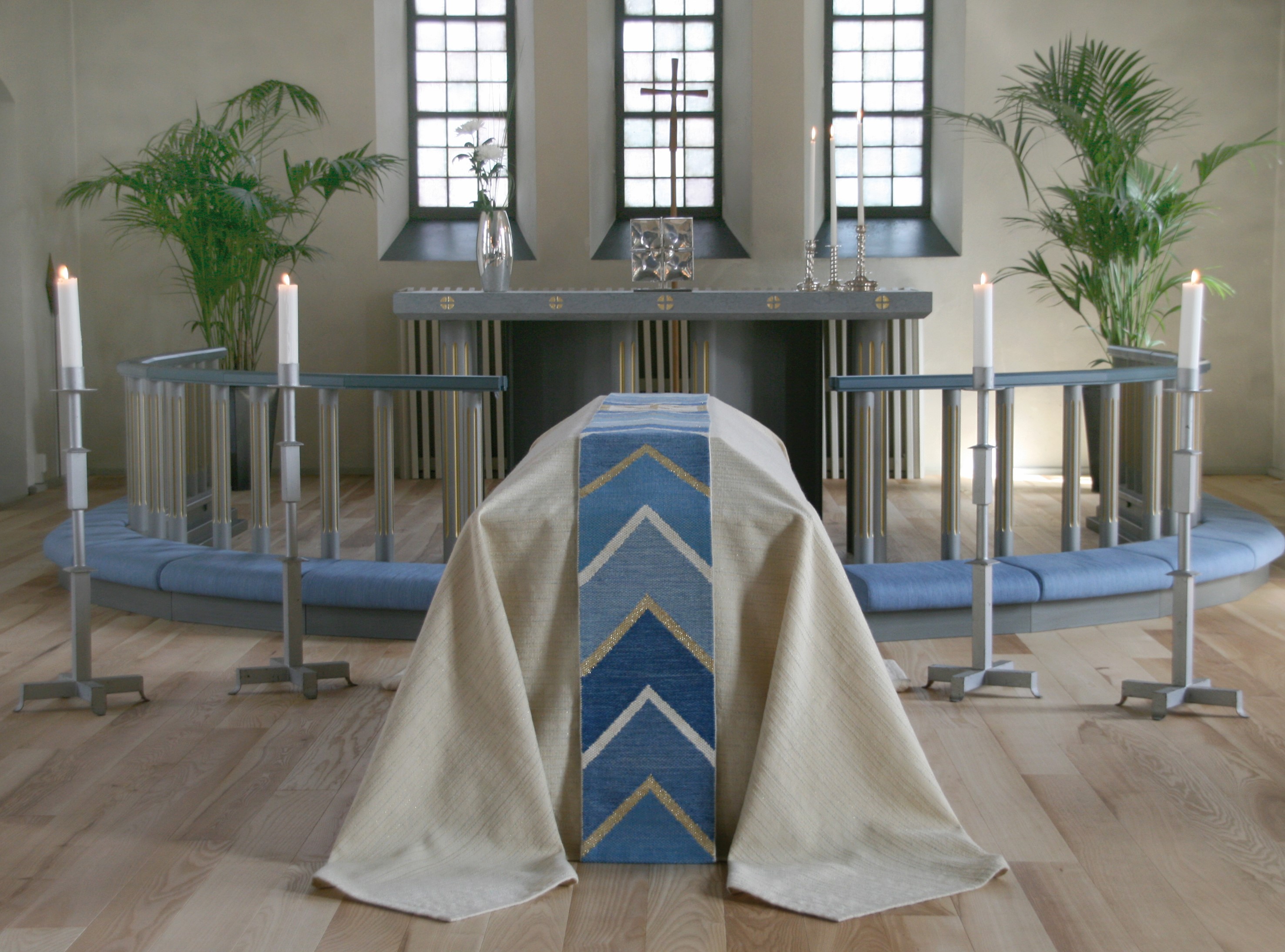 En kista står framför altaret i Tidaholms kyrka, med ett vitt bårtäcke och en blå, vit och silvrig bård ovanpå.
