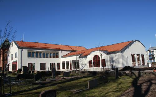 Kyrkans hus med kyrkogården och Tidaholms kyrka till vänster (utanför bilden), solen skiner och himlen är blå.