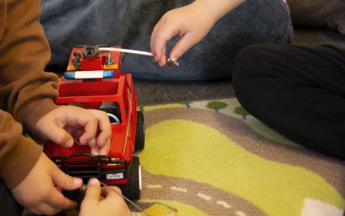 Några barn leker med en röd leksakslastbil på Öppet hus i Tidaholm, på golvet syns en matta med målade bilvägar.