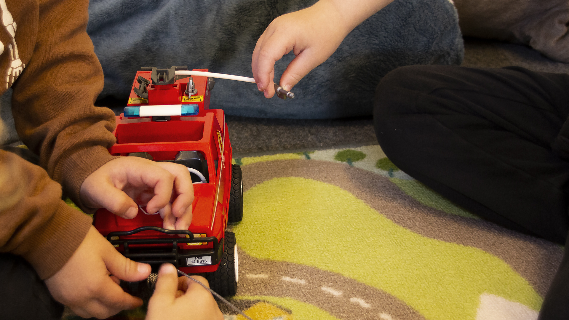 Några barn leker med en röd leksakslastbil på Öppet hus i Tidaholm, på golvet syns en matta med målade bilvägar.