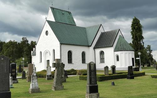 Köpinge kyrka med gröna träd i bakgrunden och svarta moln på himmelen.