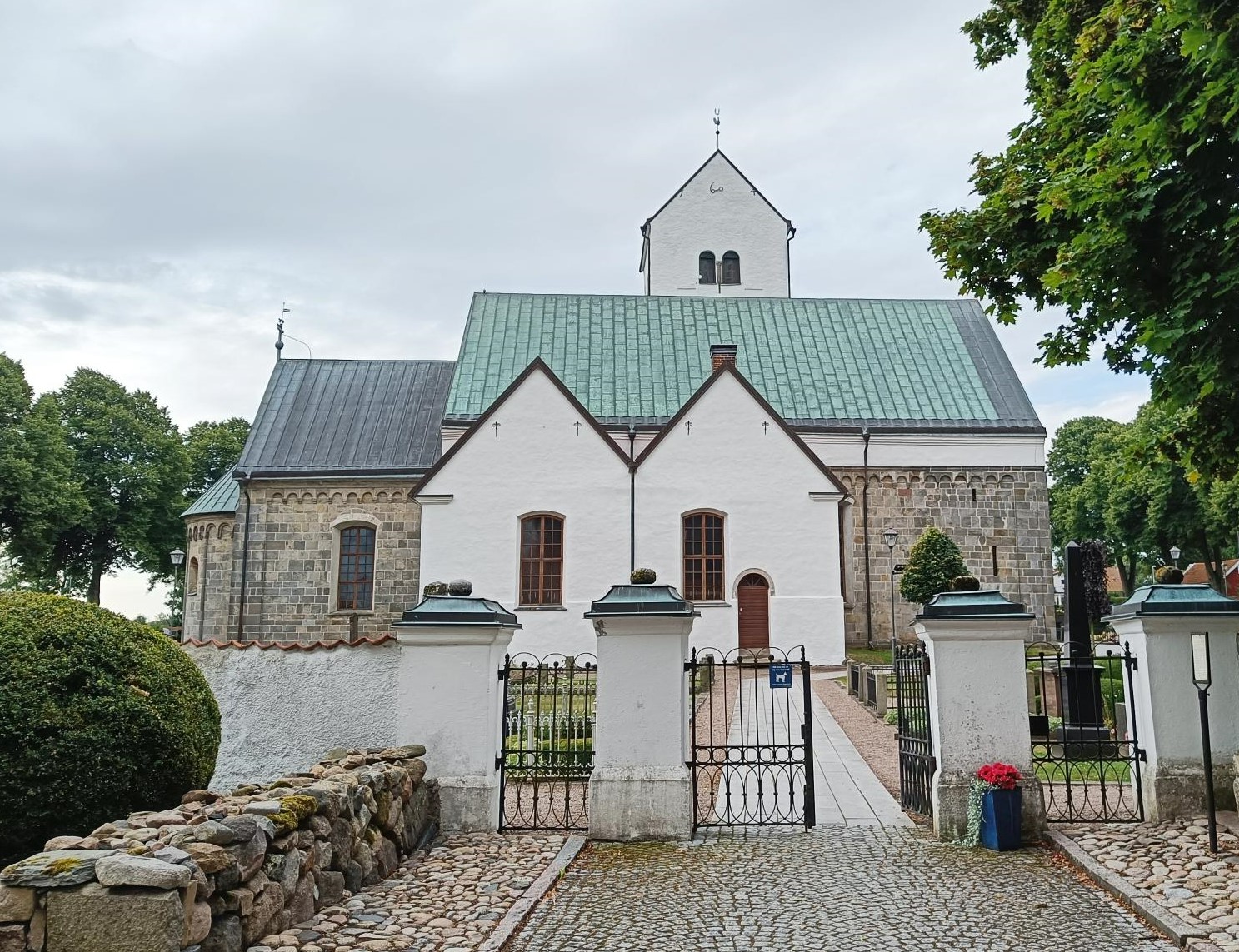 Ingång genom kyrkmur mot vit kyrka.