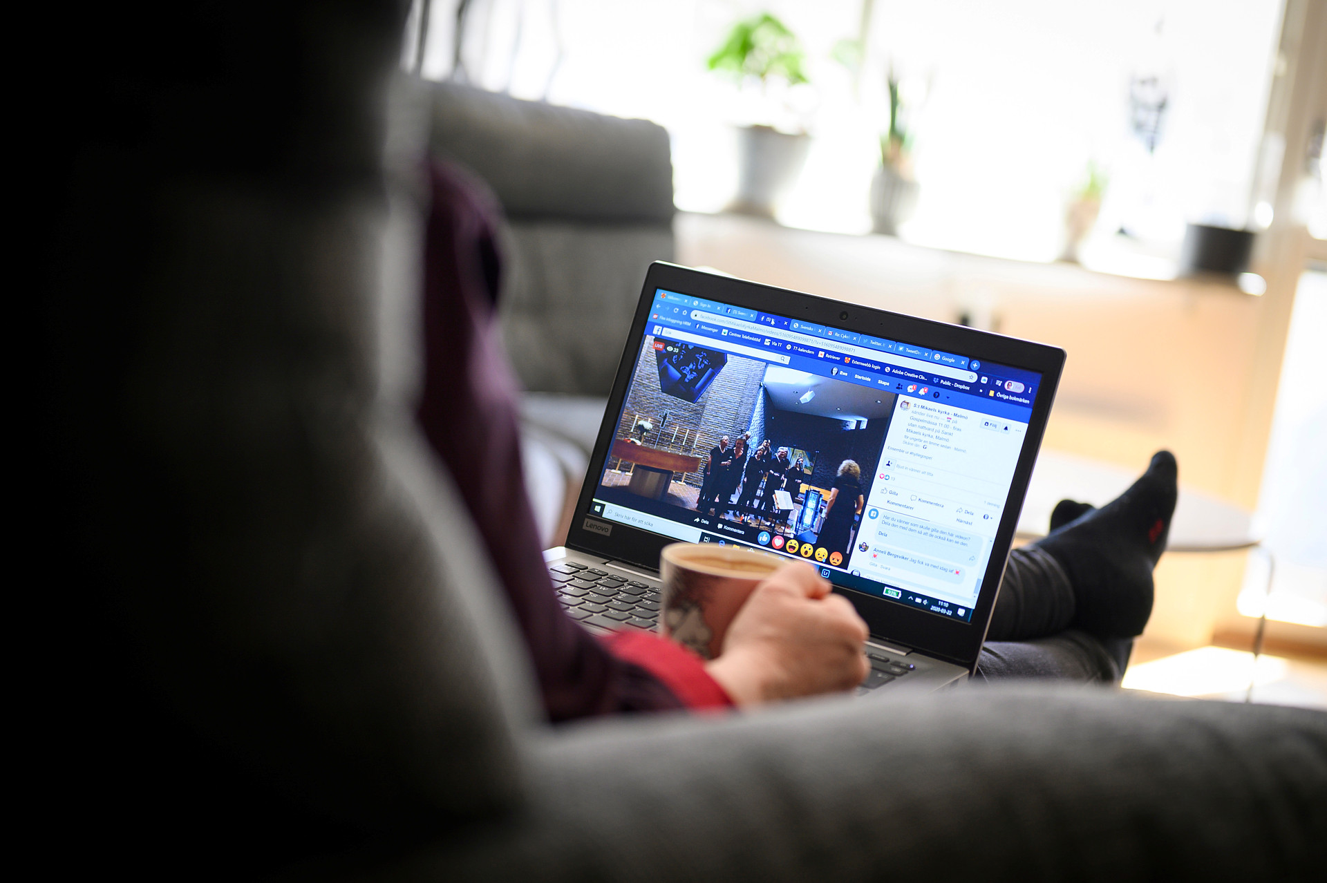 Person med kaffekopp som tittar på en digital gudstjänst på en laptop.
