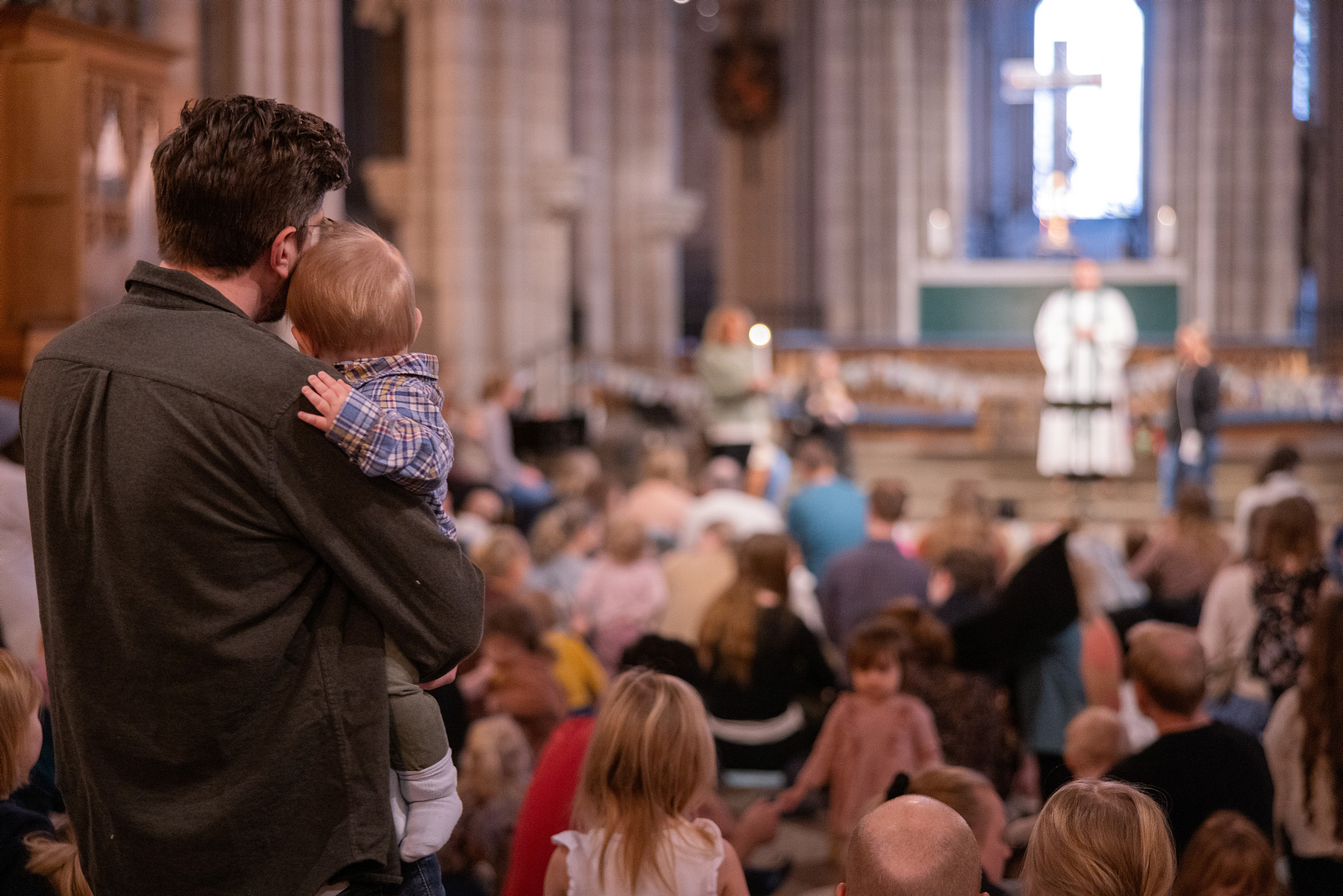 Barnmässa i Uppsala domkyrka. En pappa håller sitt lilla barn i famnen medan de blickar mot prästen som står vid altaret.