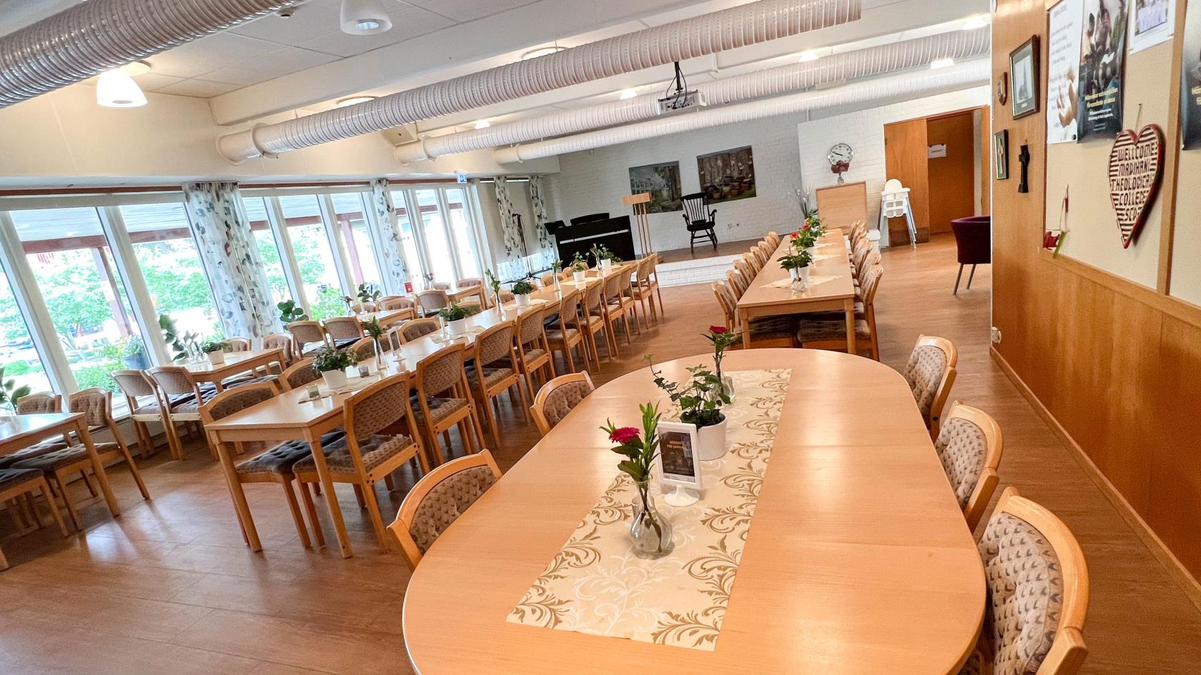 Samlingssalen i Söderledskyrkan. Närmast i bild står en rundat stort bord, längre in står långbord och till vänster står små bord utställda. På borden finns dukar och blommor utplacerade.