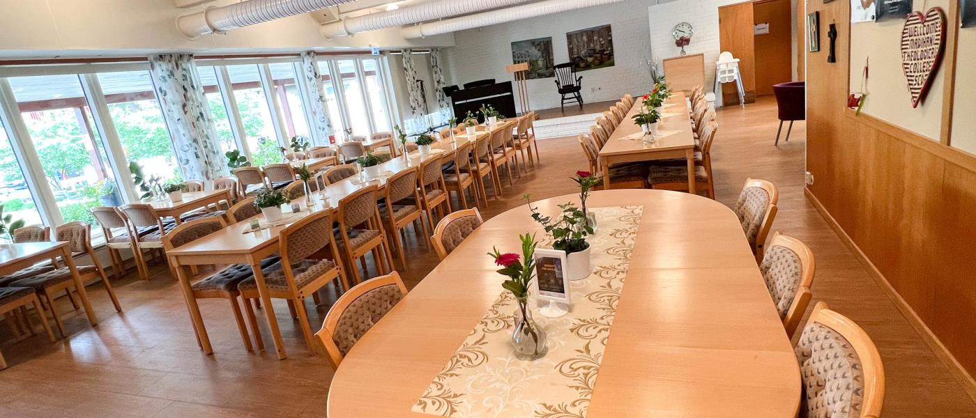 Samlingssalen i Söderledskyrkan. Närmast i bild står en rundat stort bord, längre in står långbord och till vänster står små bord utställda. På borden finns dukar och blommor utplacerade.