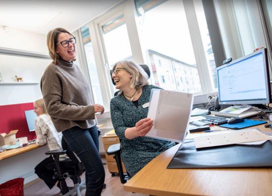 Lena vid sitt skrivbord, med prästen Elisabet i i glatt samtal