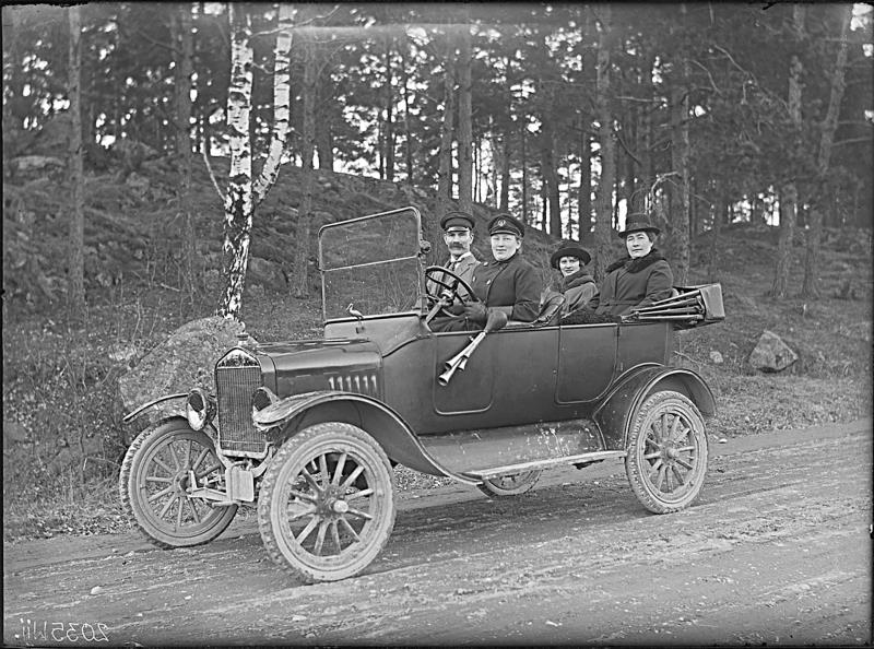 Bakom ratten sitter Hilda Pihlgren, även känd som Pila-Britta. Hon var under lång tid barnmorska i Västerås. T-forden var hennes egen. Vid hennes sida sitter Gustaf Halvar Ekstam och i baksätet hans hustru Anna Sofia Ekstam samt Ellen Gunnarsson. 