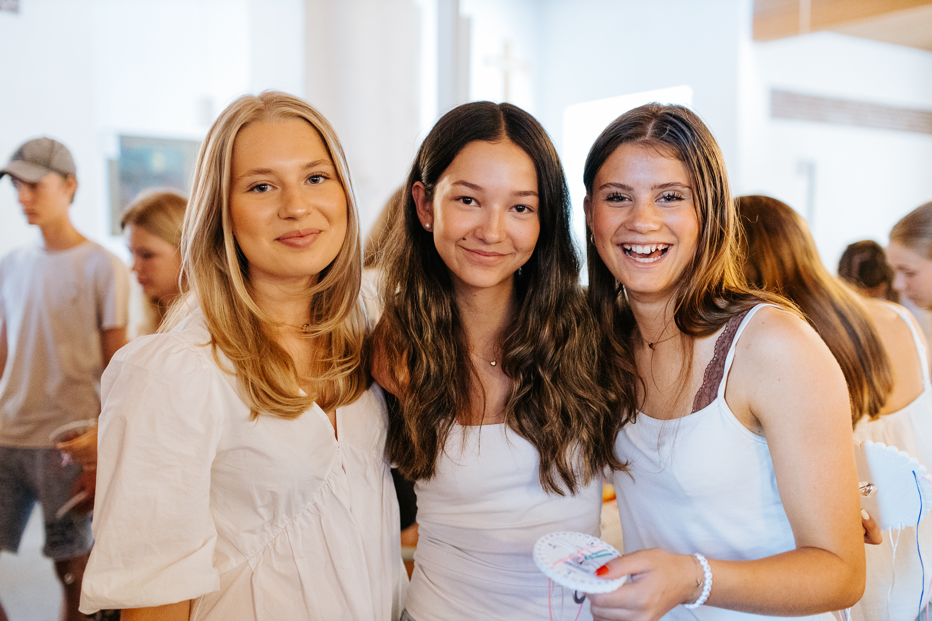 Tre sommarkonfirmander i Tomaskyrkan tittar in i kameran och ler. 