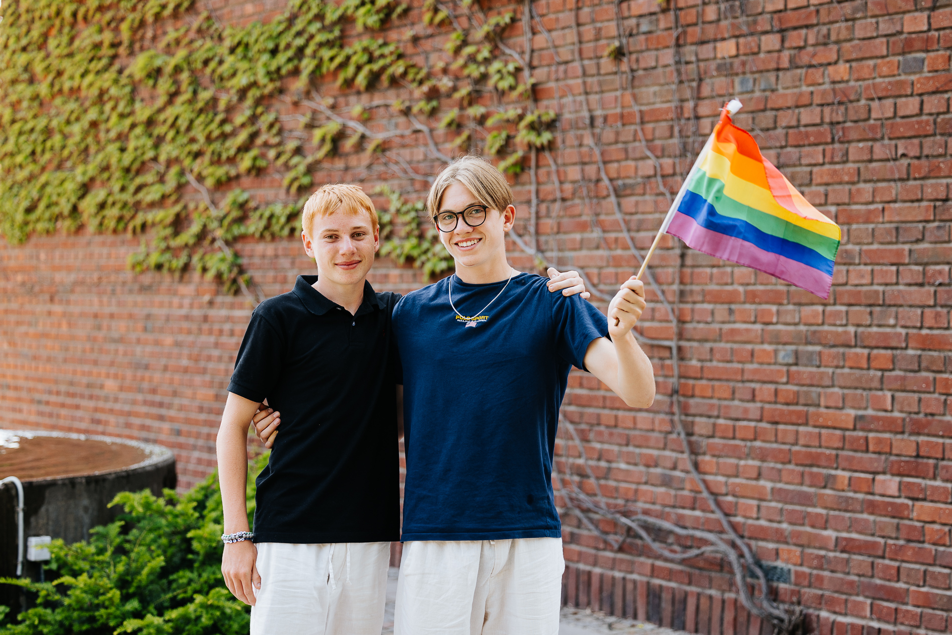 Två konfirmander vifter med en regnbågsflagga.