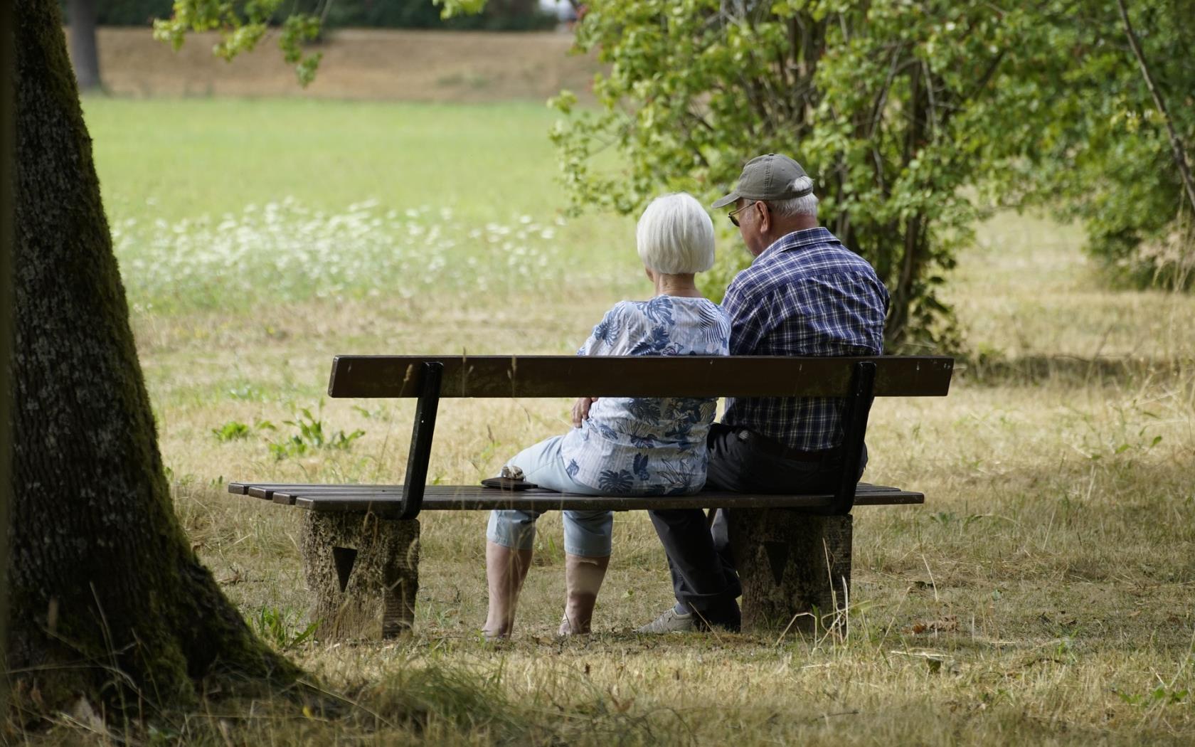 Två äldre personer sitter på en parkbänk tillsammans.