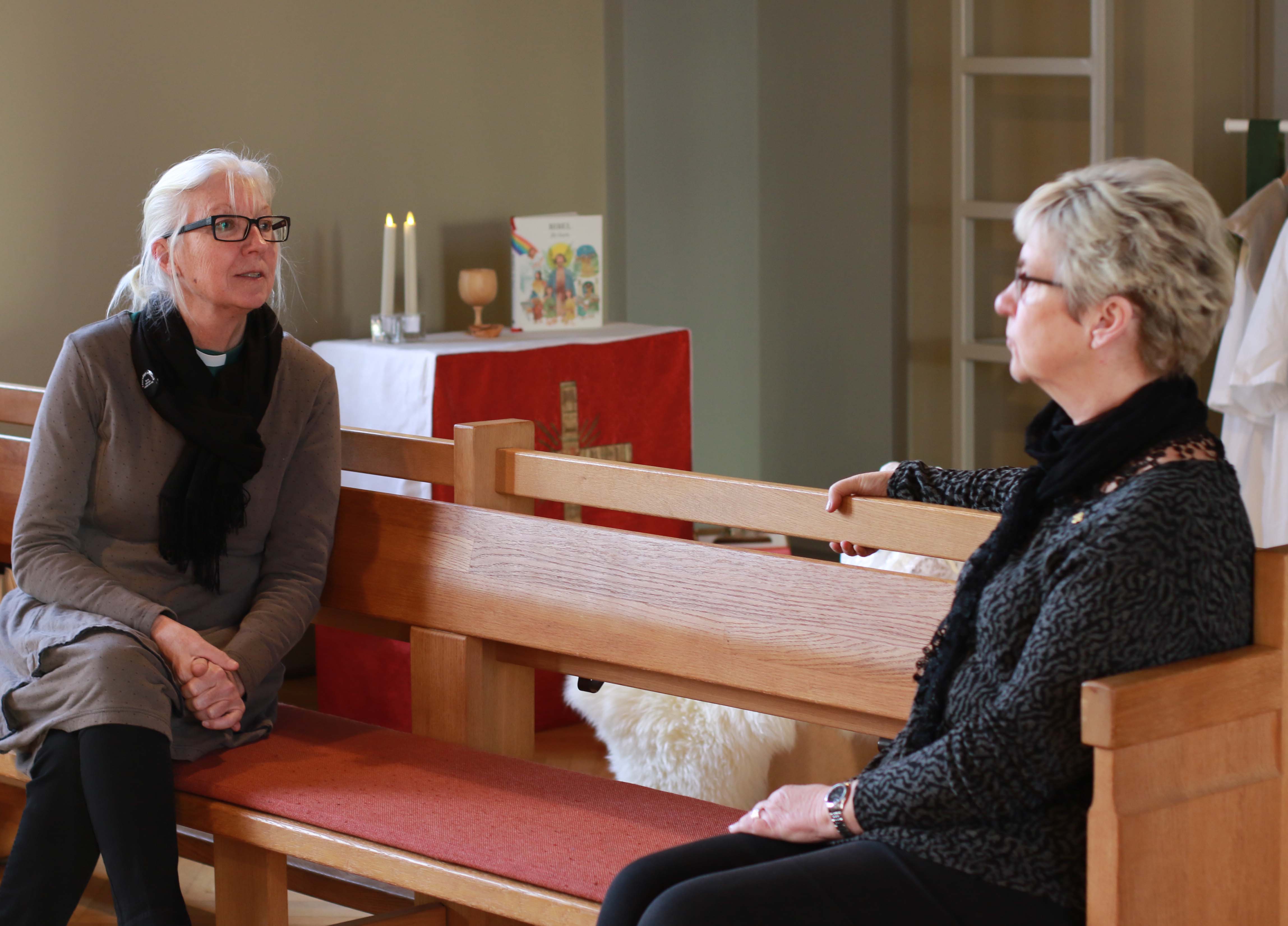 Två kvinnor i en kyrkbänk som samtalar