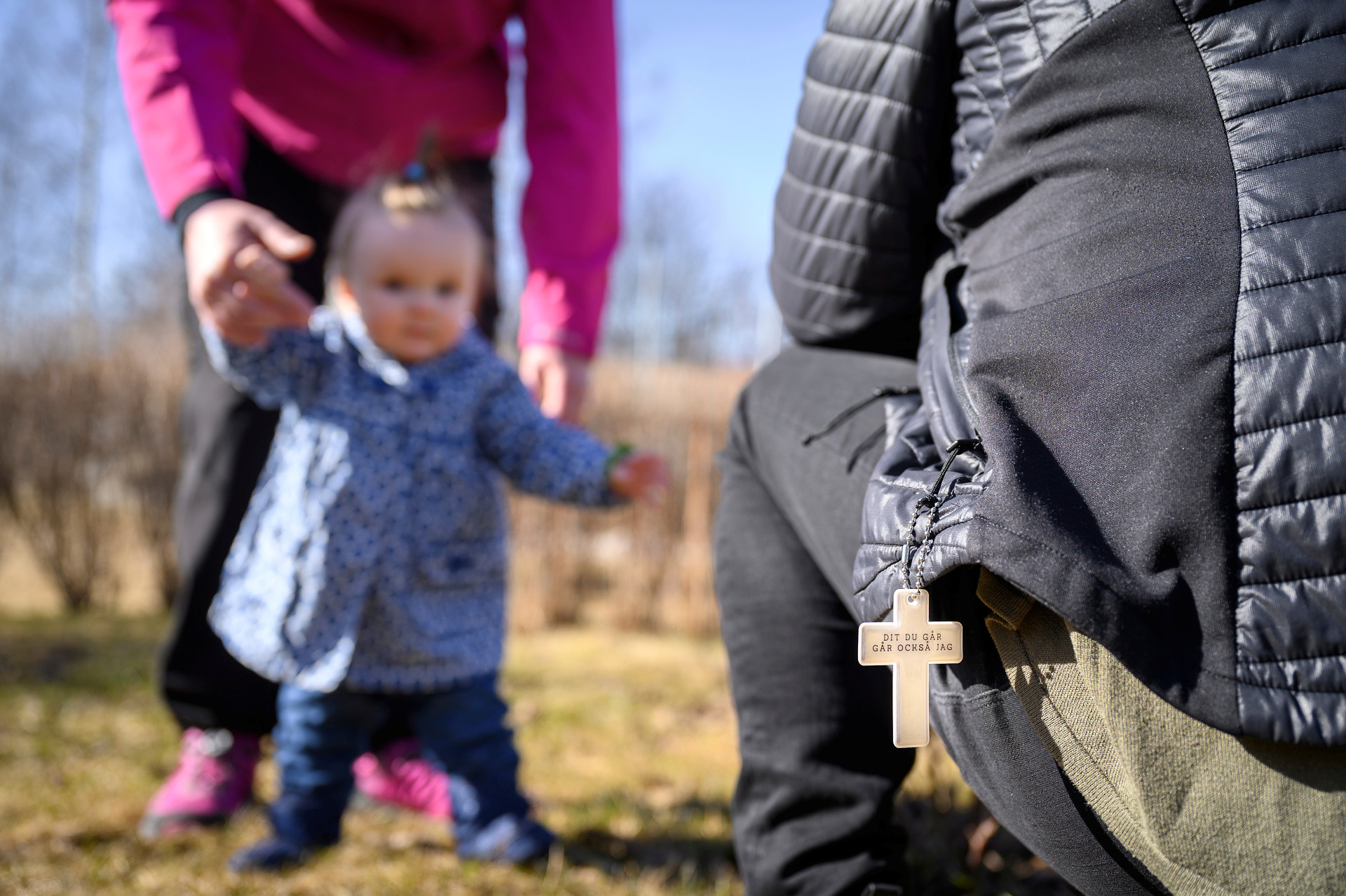 Vardagsbild på barn, förälder och en person till. Ett kors med texten Dit du går går också jag