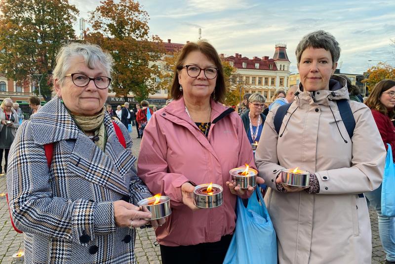 Tre kvinnor håller i tända marschaller på ett torg. 