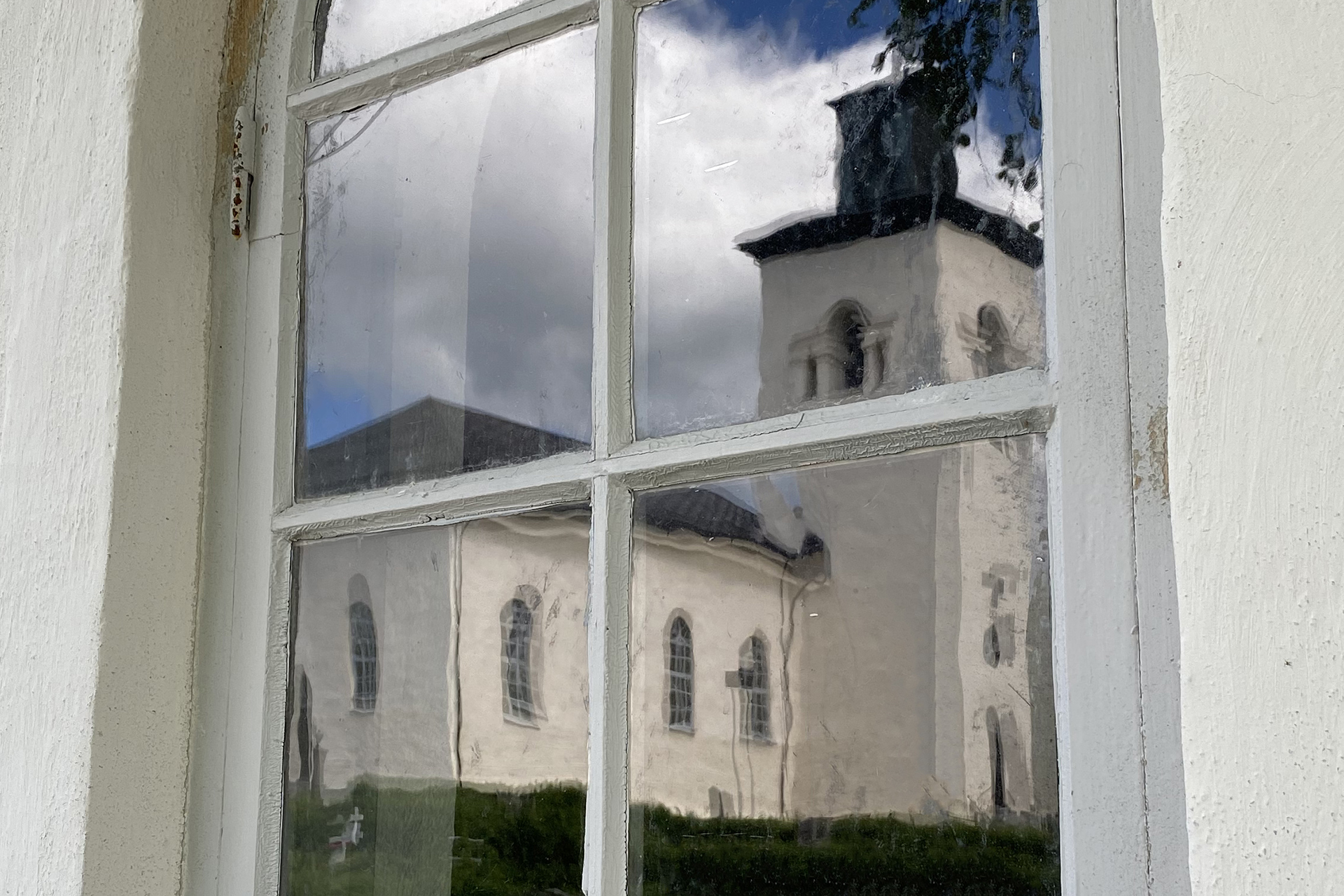 Överluleå kyrka speglas i fönstret till gravkapellet på Gamla kyrkogården.