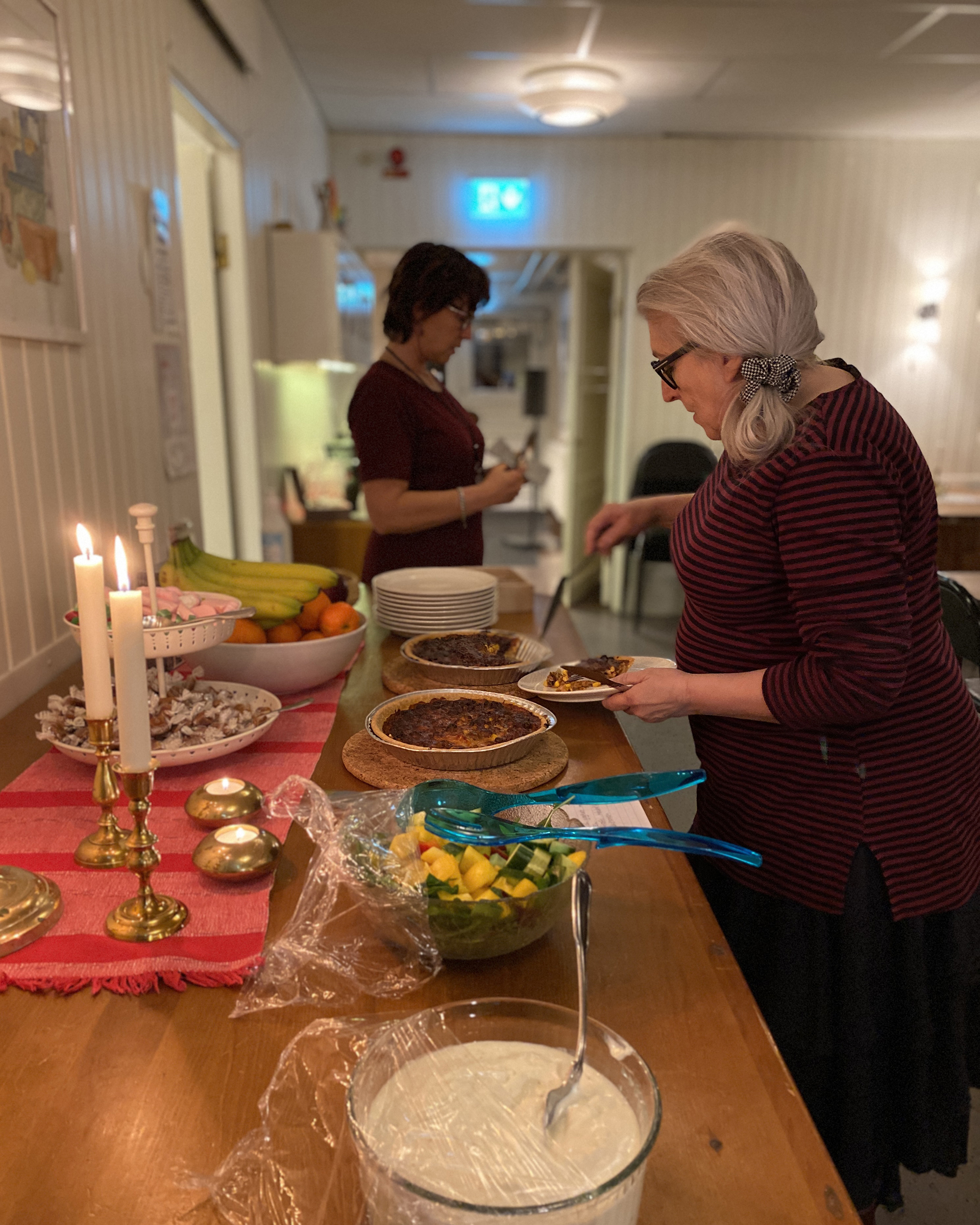 Kvinna tar mat vid en uppdukad buffe. I bakgrunden syns ytterligare en kvinna. 