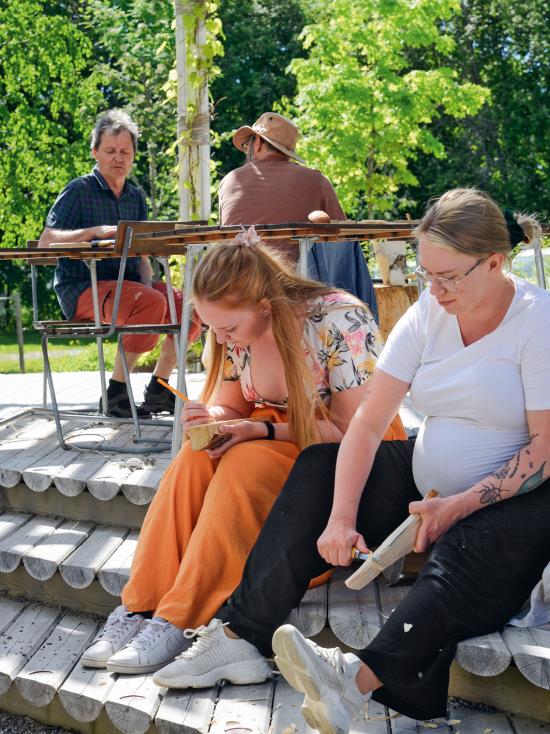 Två kvinnor sitter på altan och täljer.