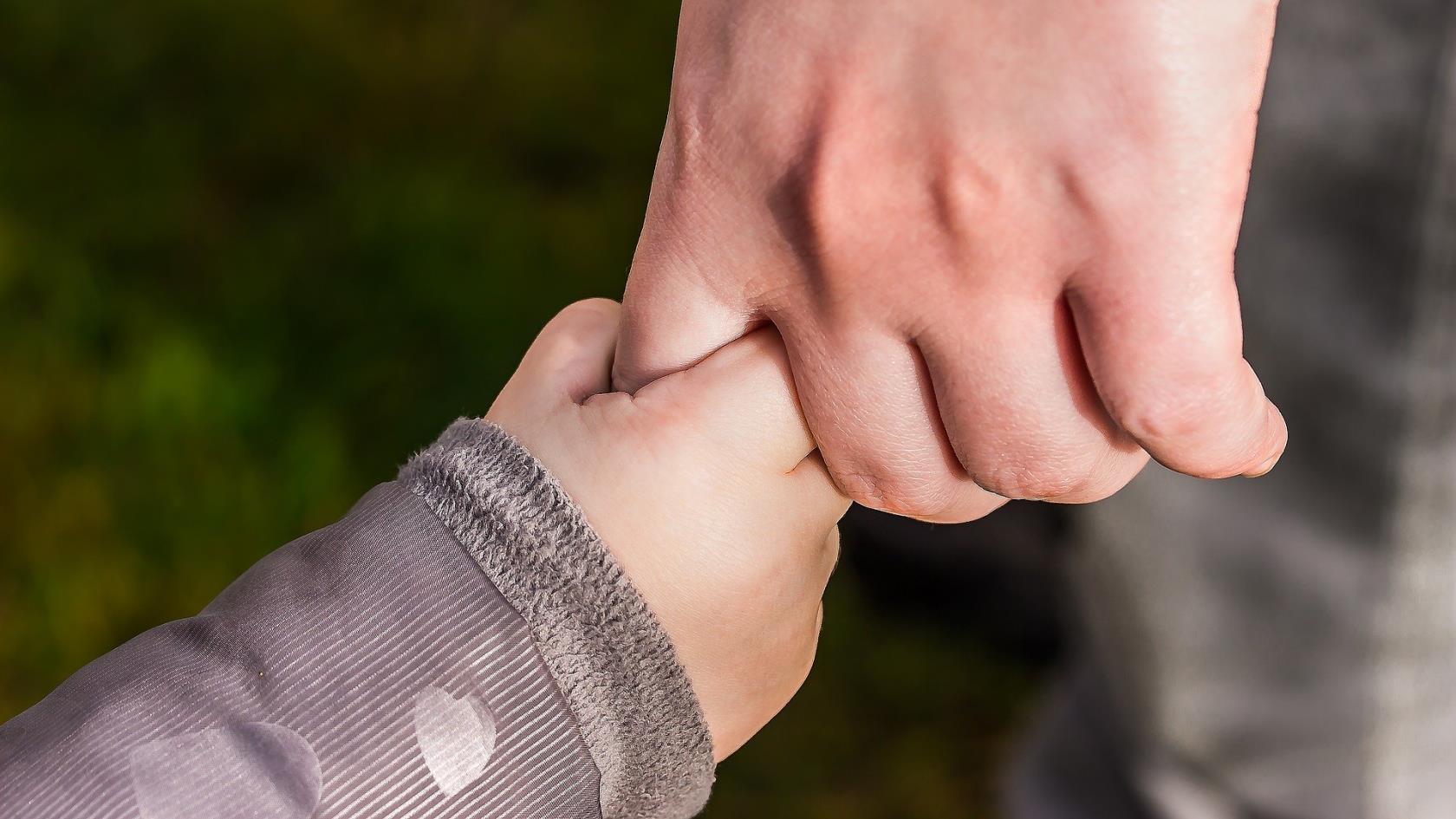 En barnhand som håller i en vuxen hand