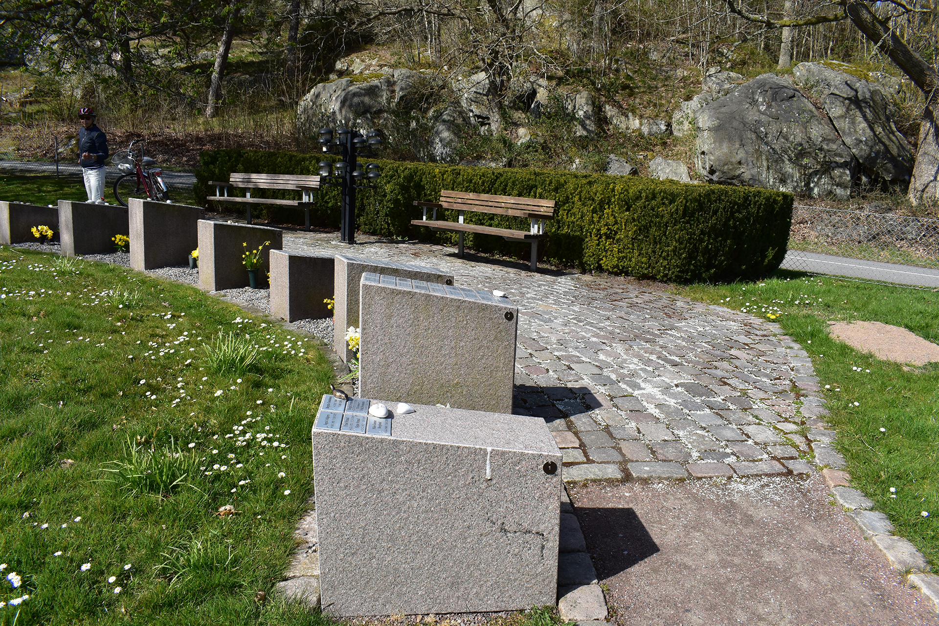 Stenlagd gång med stenstoder som rymmer namnplaketter på kyrkogård.