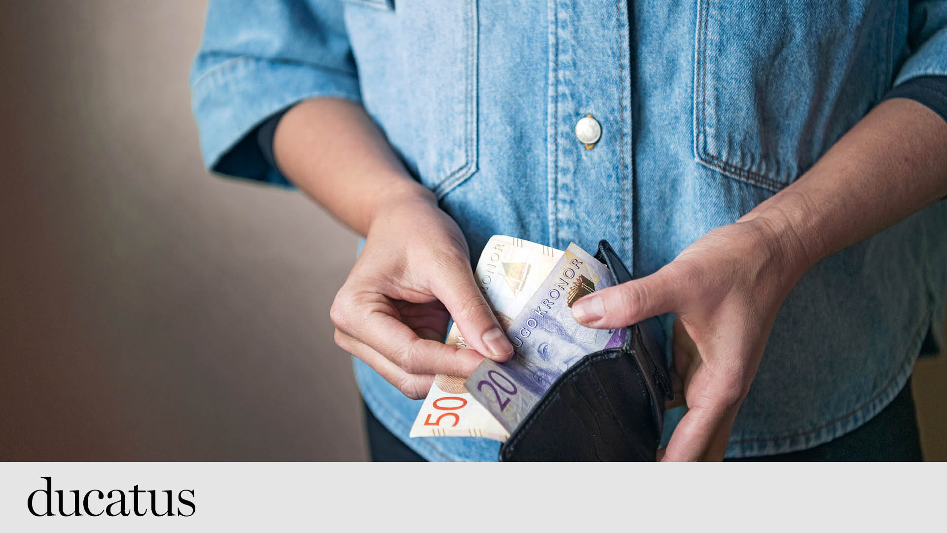 en person i jeanskjorta öppnar en plånbok och visar upp sedlar. 