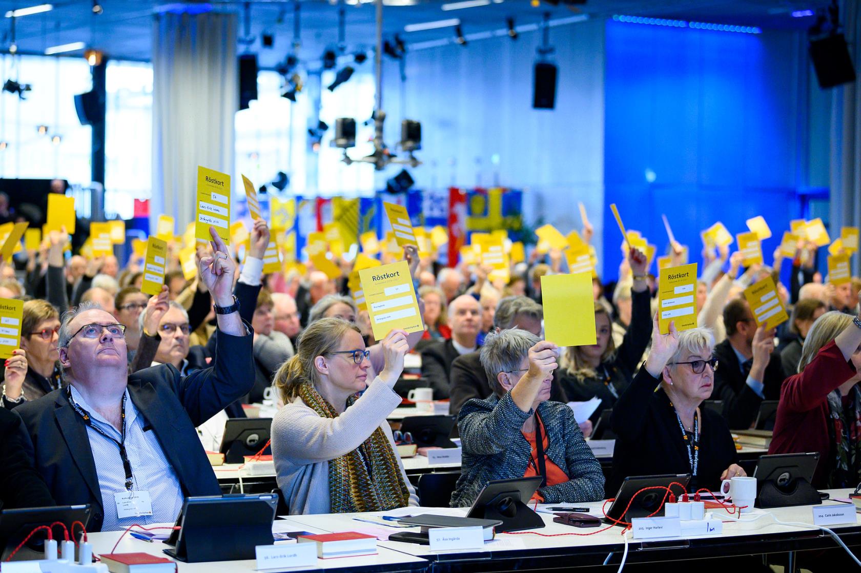 Ledamöter i kyrkomötet röstar genom att hålla upp  gula  lappar i kyrkomötets andra session 2019