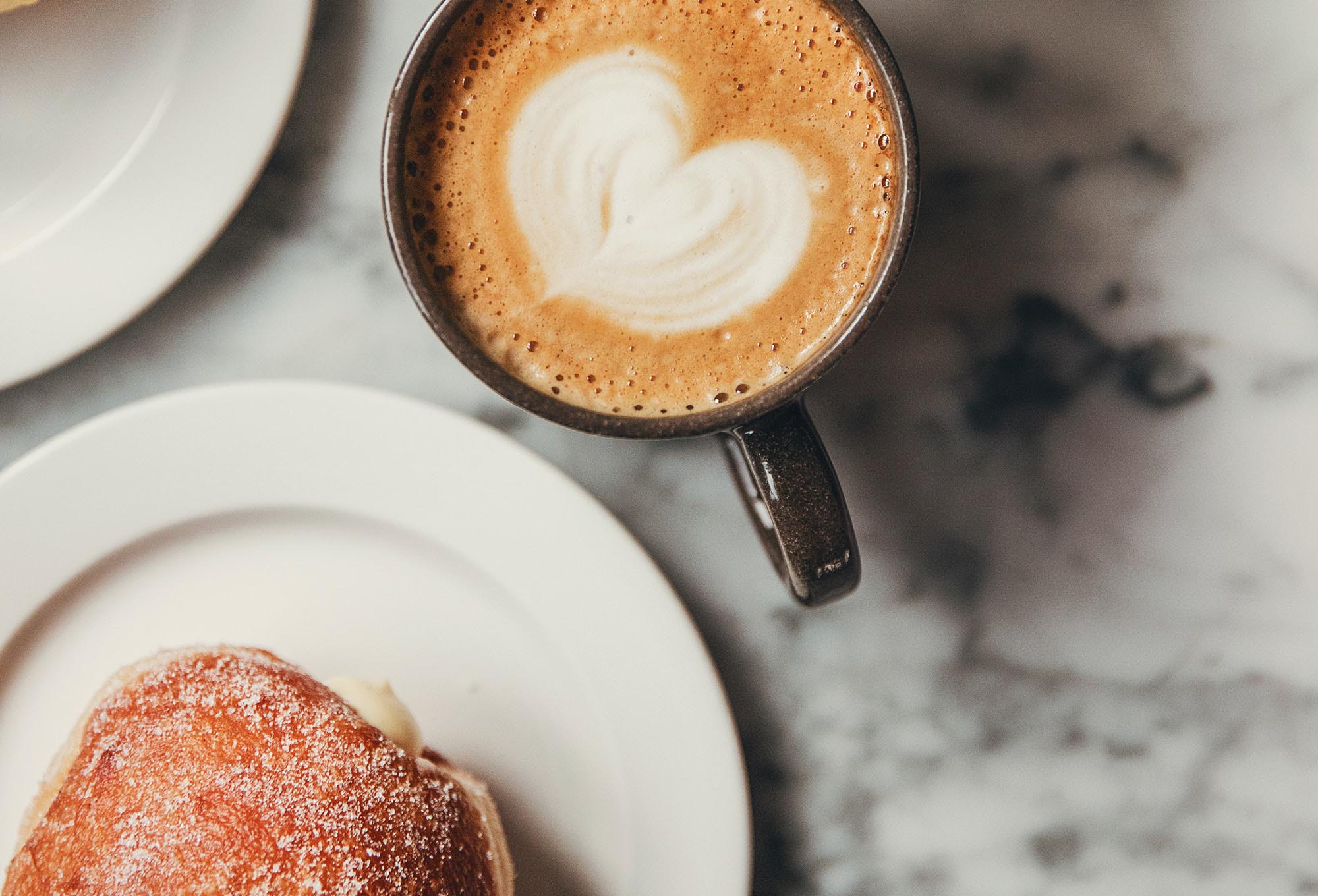 Kaffe med ett hjärta i mitten och en bulle.