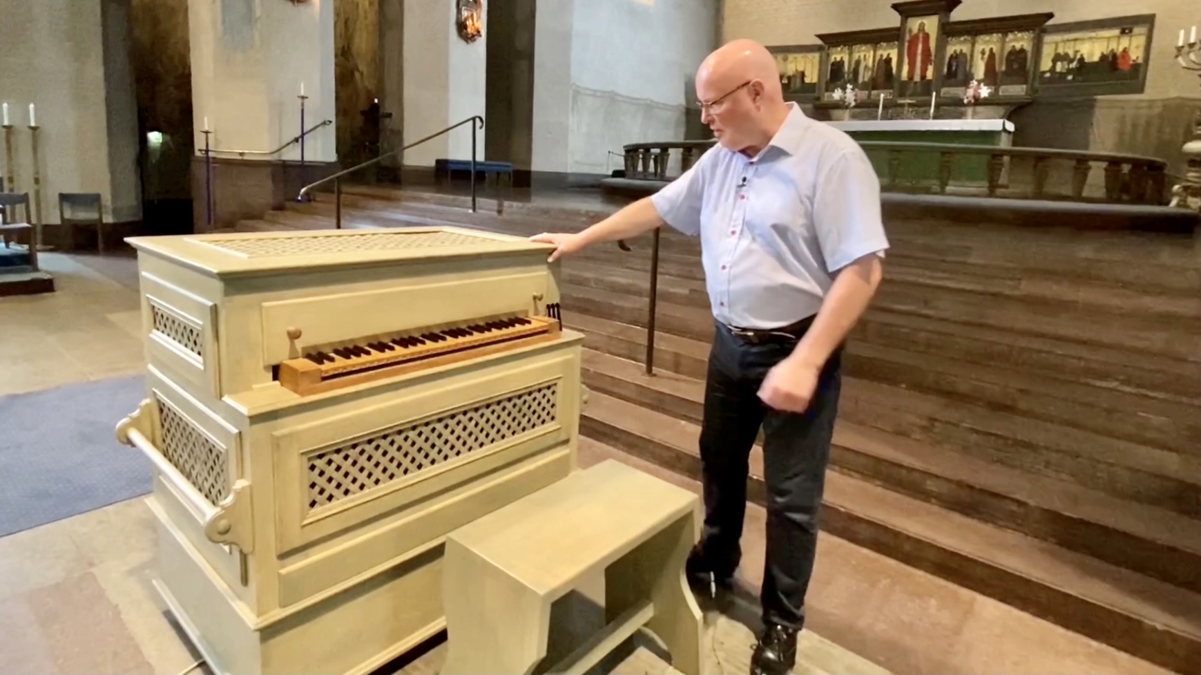 En liten beigefärgad orgel.  En man står bredvid och håller ena handen på orgeln. 
