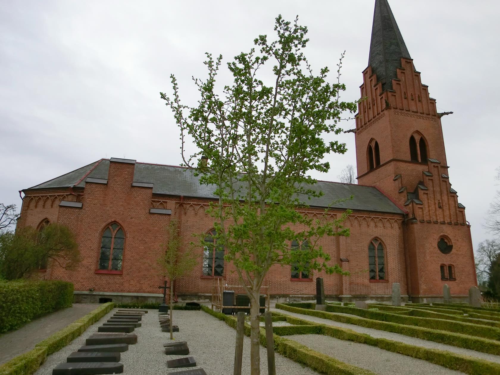 Röd tegelkyrka med långhus och torn.