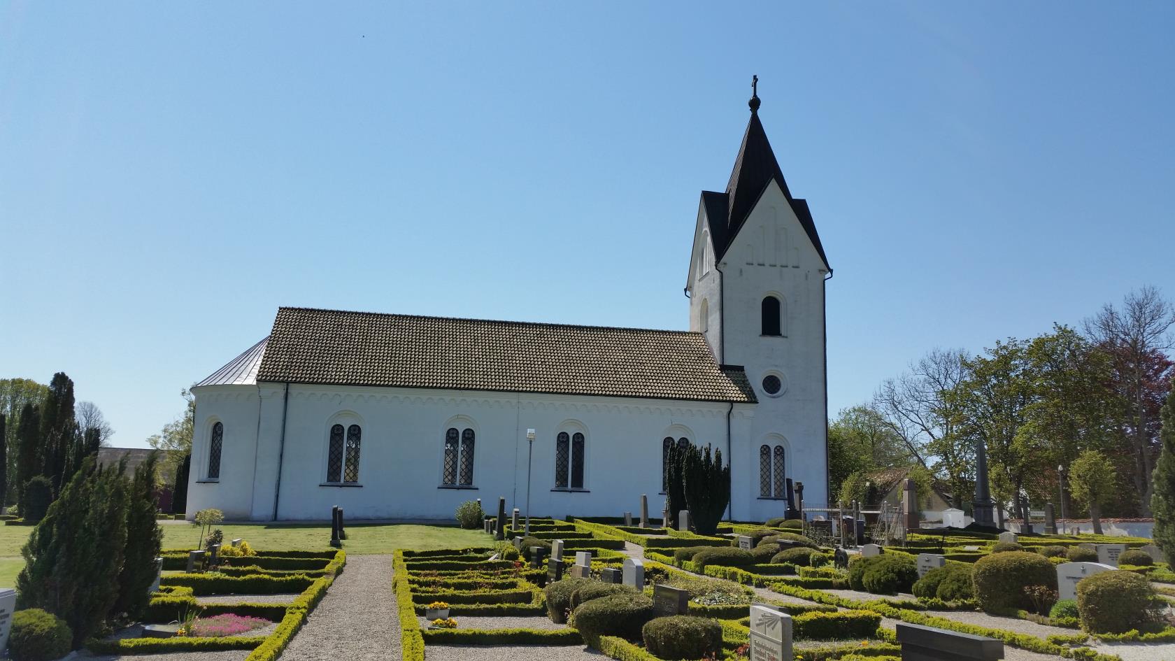 Vit kyrka med långhus och torn.