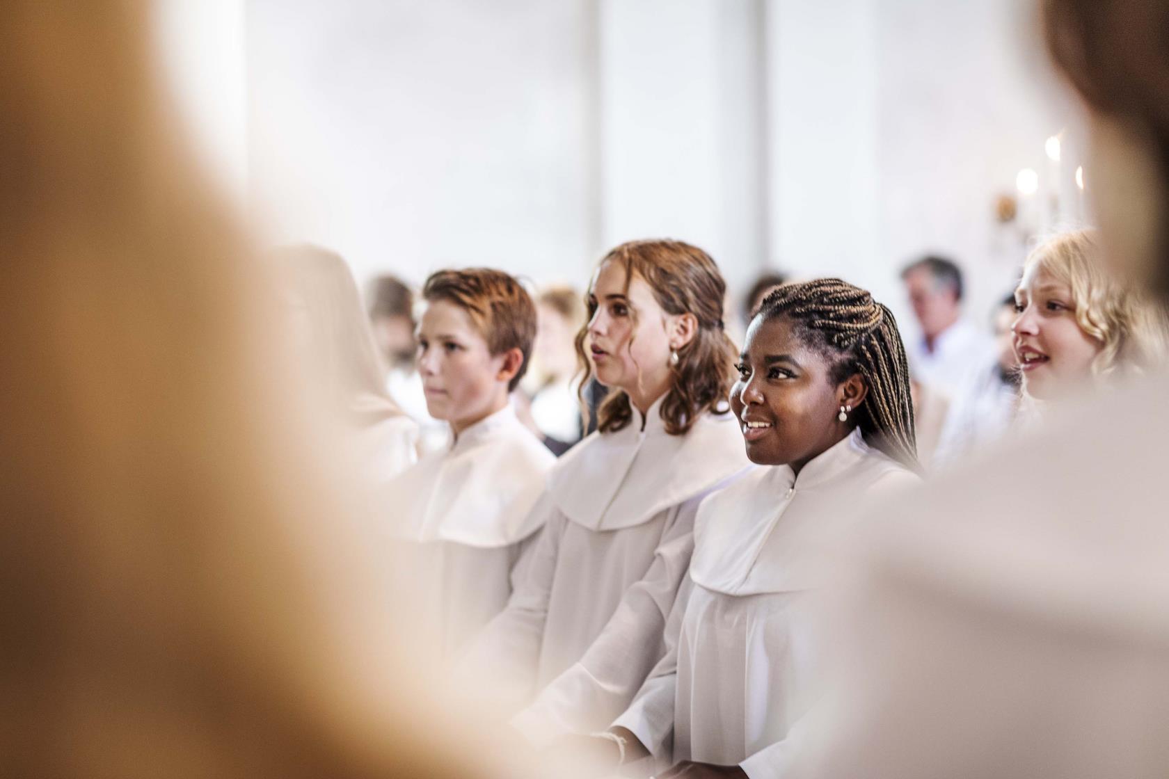 Konfirmander i vita kåpor i en kyrka.