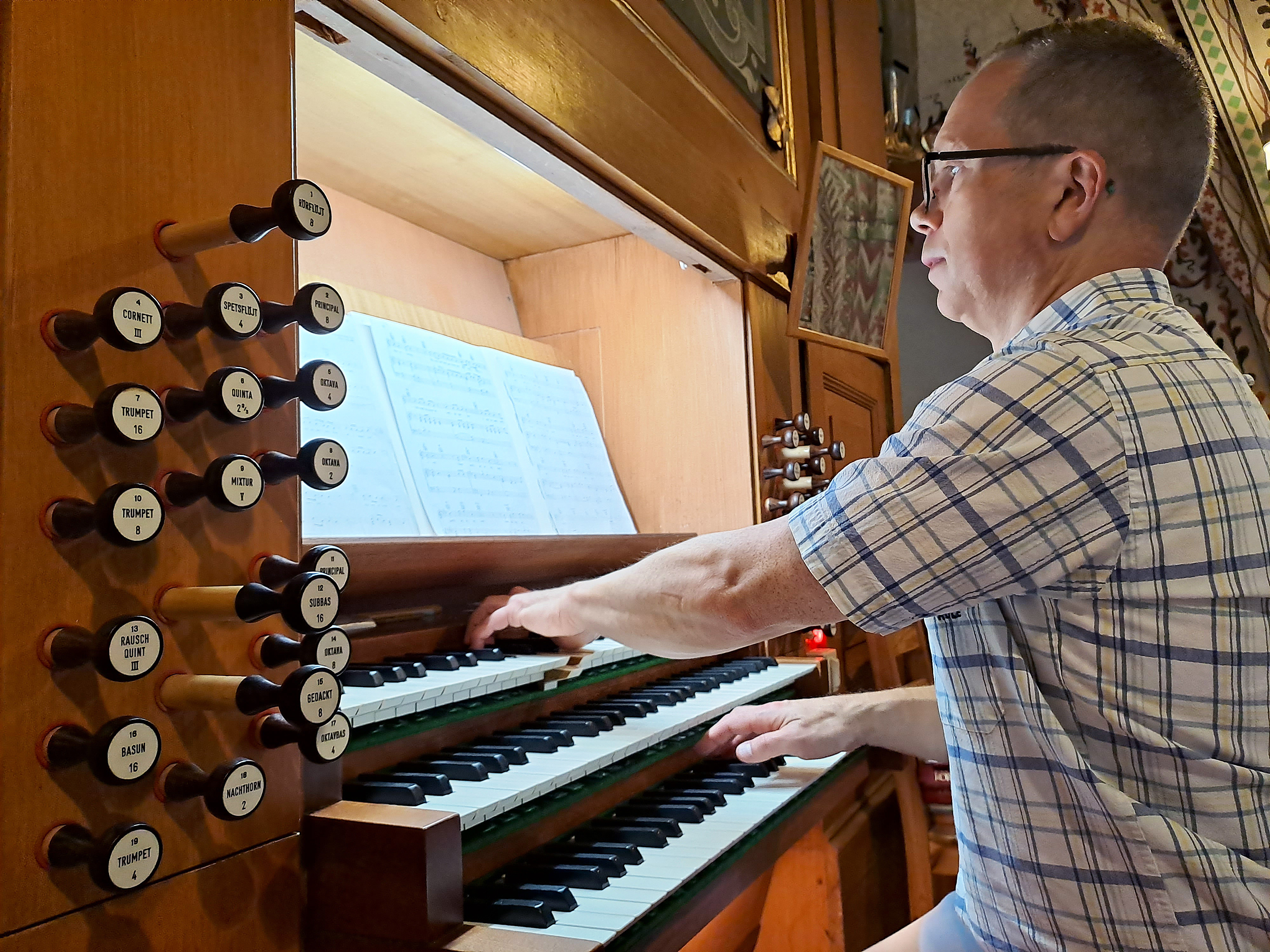 En man med glasögon spelar på en kyrkorgel.