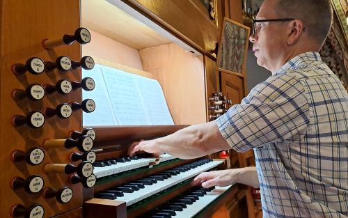 En man med glasögon spelar på en kyrkorgel.