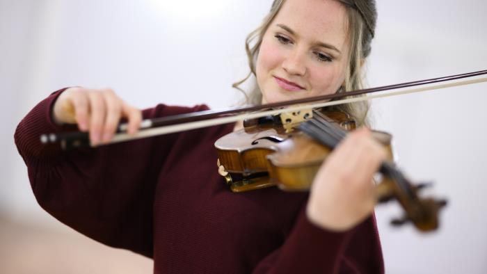 En ung tjej i mörkröd klänning spelar fiol. Hon ser fokuserad ut.