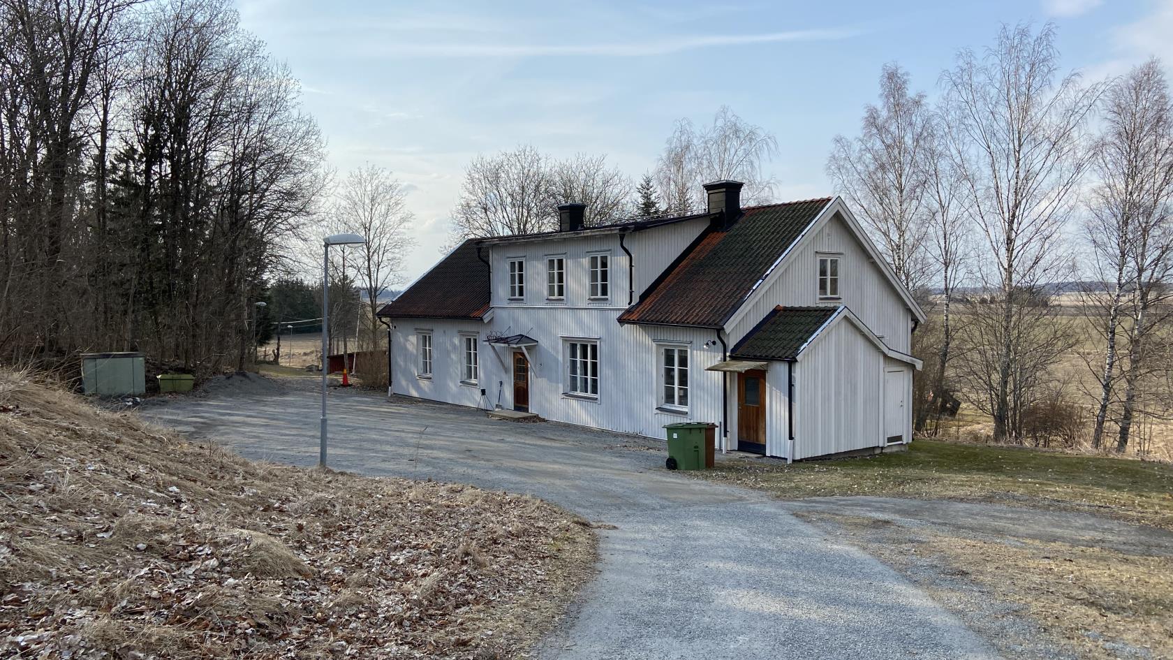 En grusväg leder ner till ett vitt hus.