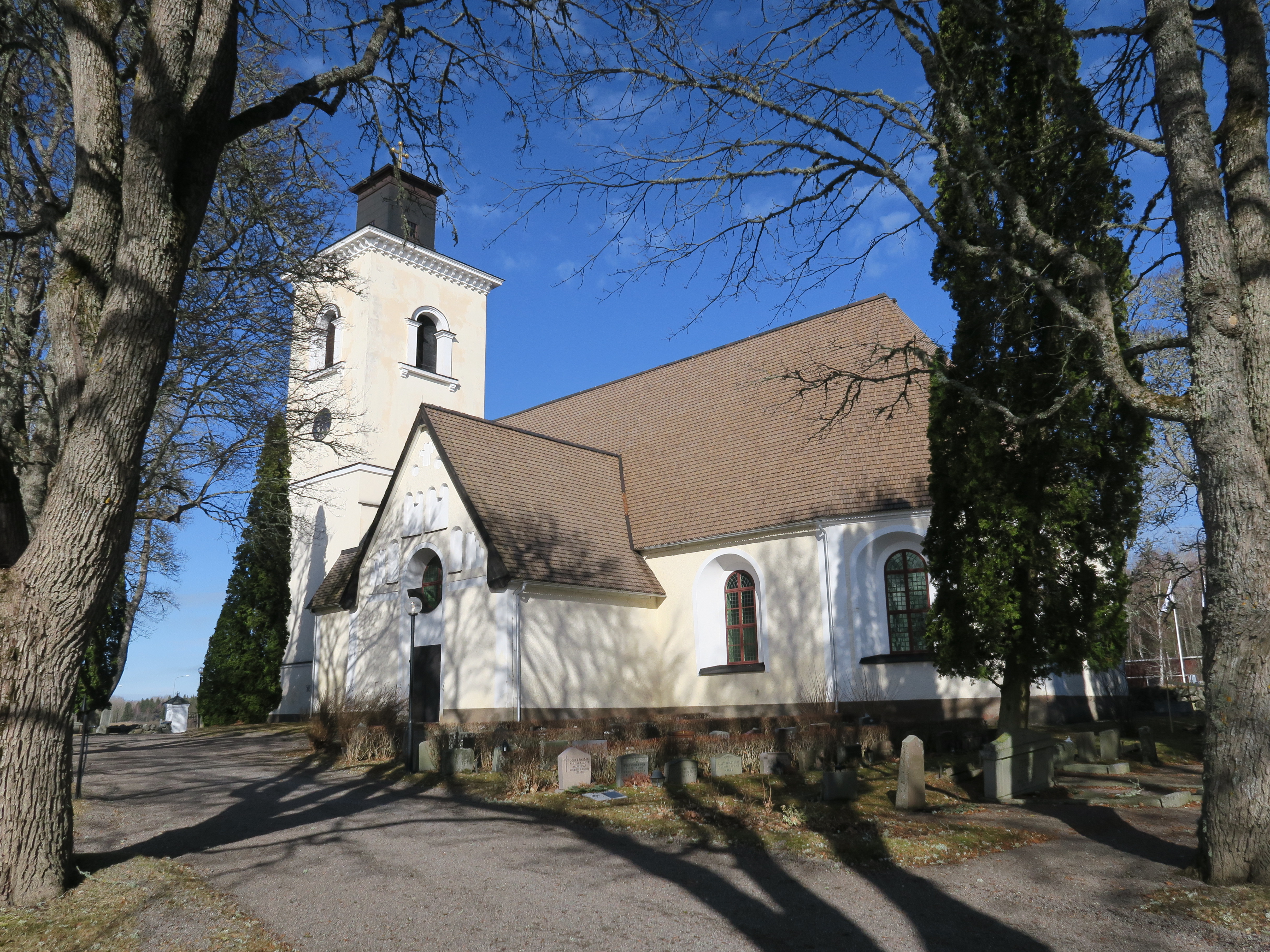 En vit kyrka med ett torn, omgiven av träd.