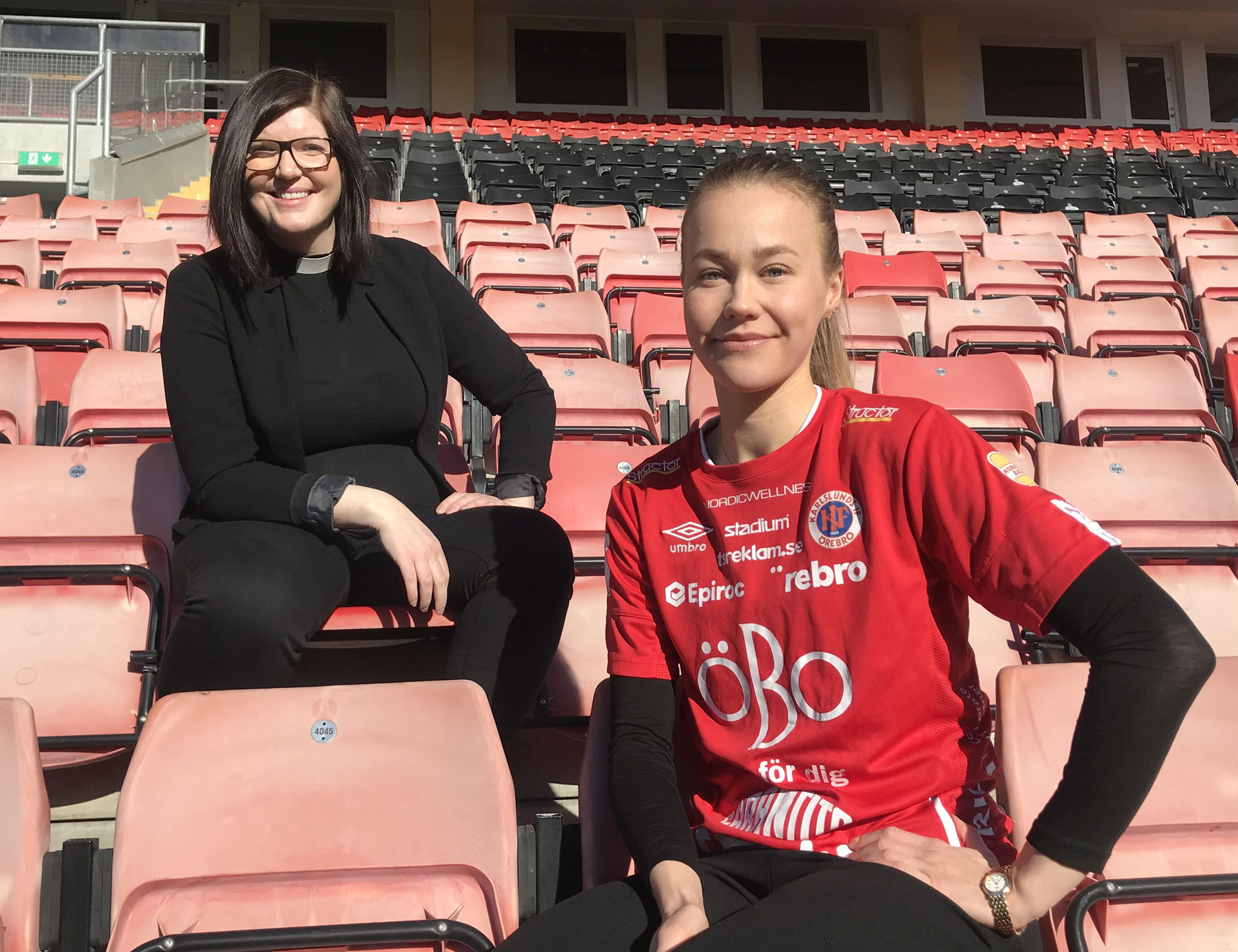 Bilden visar citypräst Sara Nässelqvist och Frida Abrahamsson som är lagkapten för KIF Örebro DFF. De sitter på läktaren på Behrn Arena.